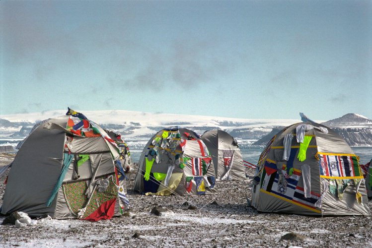Four tents pitched in a snowy, barren landscape are doeorated with flags, gloves, and clothing.
