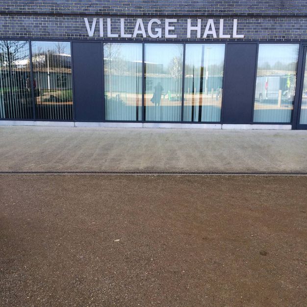 Architecture. A long building with the sign “Village Hall” is above a bank of windows.